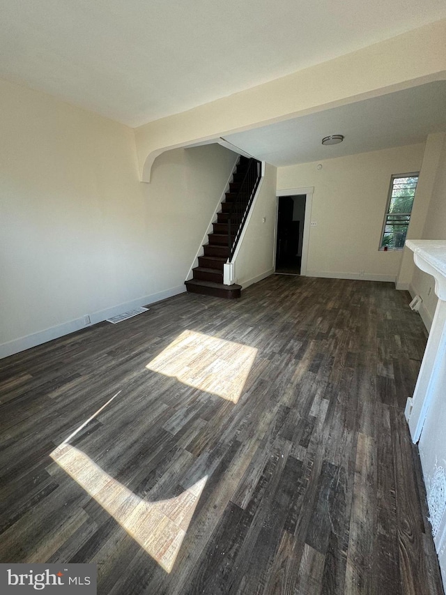 unfurnished living room featuring dark wood finished floors, stairway, and baseboards