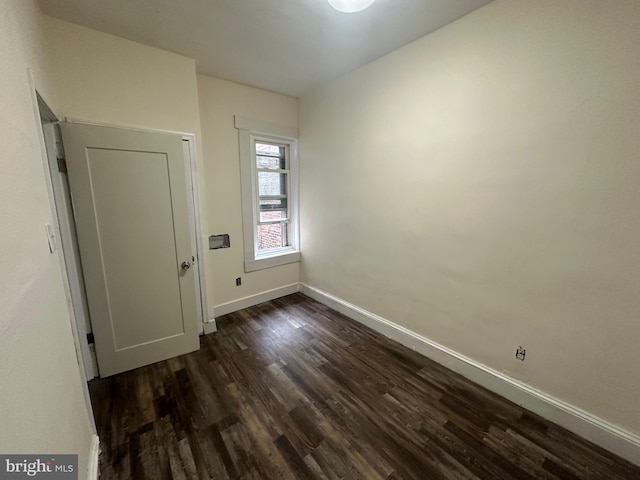 unfurnished room with baseboards and dark wood-style floors