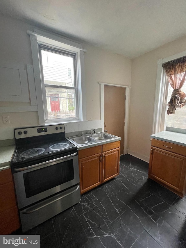 kitchen featuring light countertops, brown cabinets, stainless steel range with electric stovetop, marble finish floor, and a sink