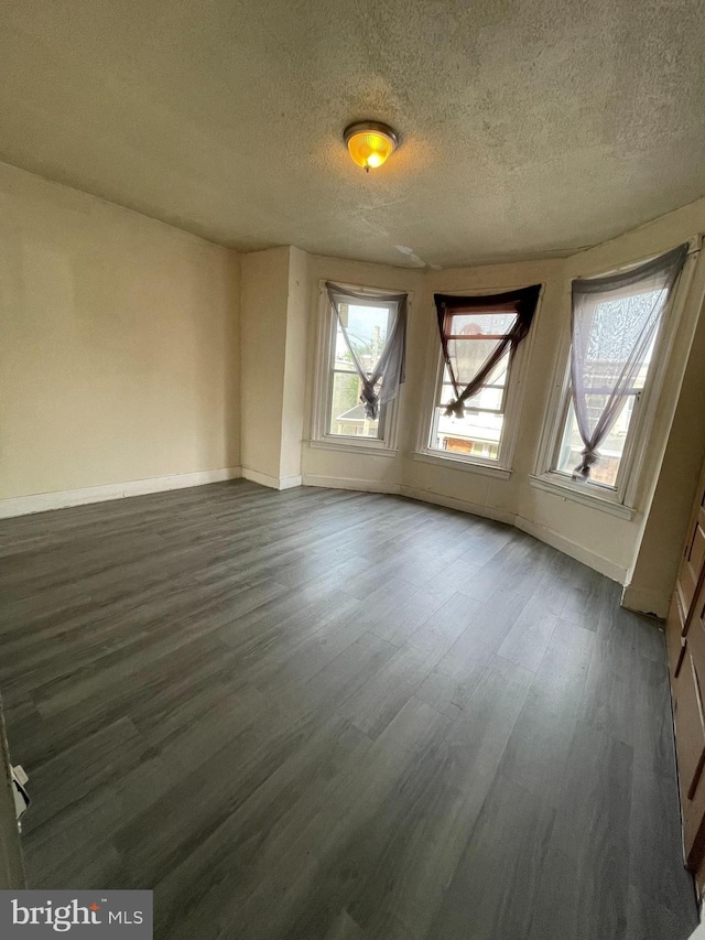 empty room featuring baseboards, a textured ceiling, and dark wood finished floors