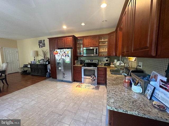 kitchen with appliances with stainless steel finishes, light wood-type flooring, light stone countertops, and sink