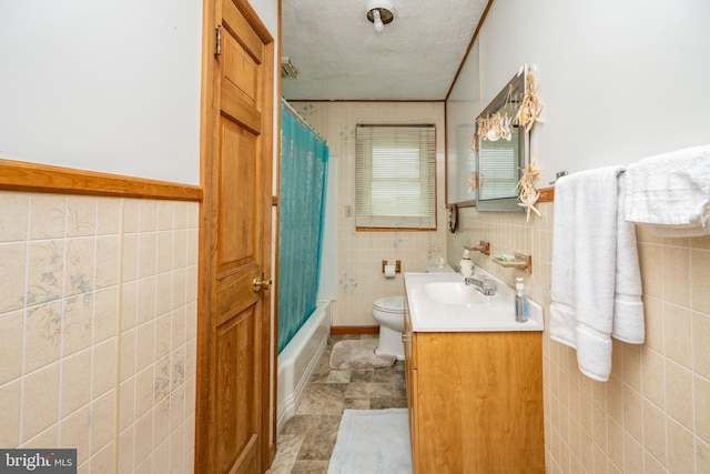 full bathroom featuring tile walls, a textured ceiling, shower / tub combo with curtain, vanity, and toilet