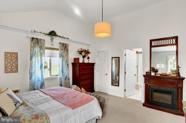 carpeted bedroom with multiple windows, a fireplace, ensuite bathroom, and vaulted ceiling