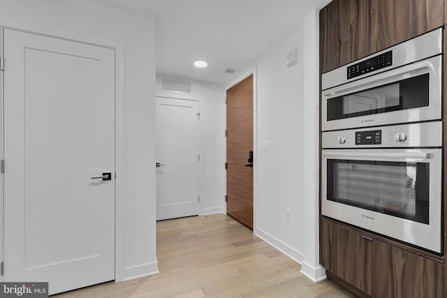 kitchen featuring stainless steel double oven, dark brown cabinetry, and light wood-type flooring