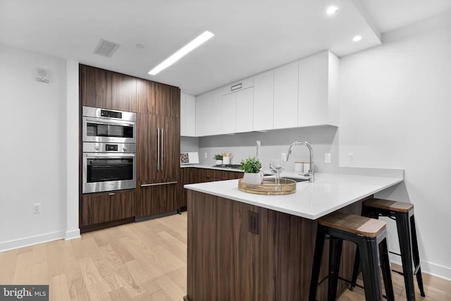 kitchen featuring stainless steel double oven, sink, light wood-type flooring, and white cabinetry