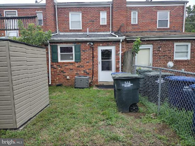 rear view of property with a storage unit, a yard, and cooling unit