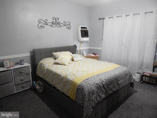 bedroom with dark colored carpet, heating unit, and wainscoting