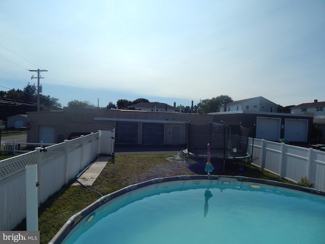 view of swimming pool with a trampoline and a fenced backyard