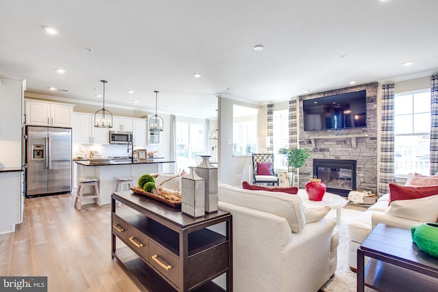 living room with an inviting chandelier, a fireplace, light hardwood / wood-style floors, and crown molding