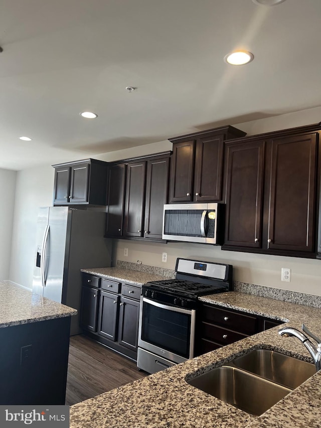 kitchen with light stone counters, dark brown cabinetry, sink, stainless steel appliances, and dark hardwood / wood-style flooring