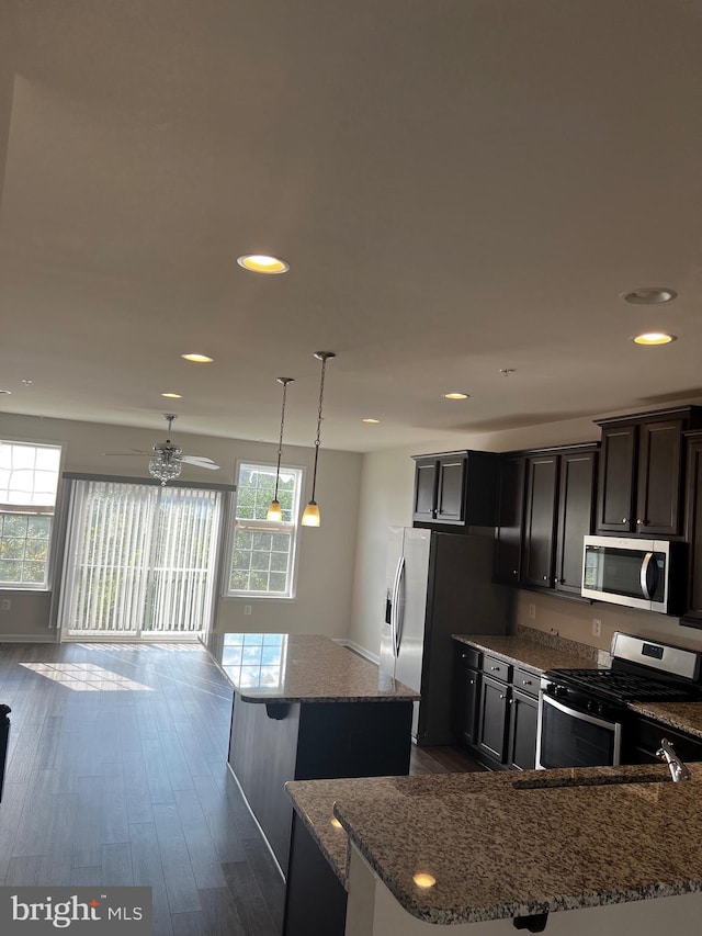 kitchen featuring a center island, hanging light fixtures, stainless steel appliances, dark hardwood / wood-style flooring, and light stone countertops