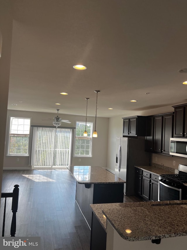 kitchen featuring hanging light fixtures, dark hardwood / wood-style flooring, stone countertops, stainless steel appliances, and a center island