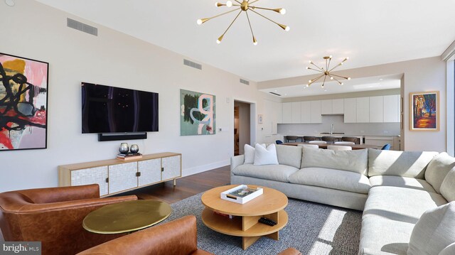 living room with dark wood-type flooring, an inviting chandelier, and sink