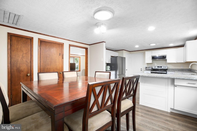 dining area featuring crown molding, a textured ceiling, hardwood / wood-style flooring, and sink