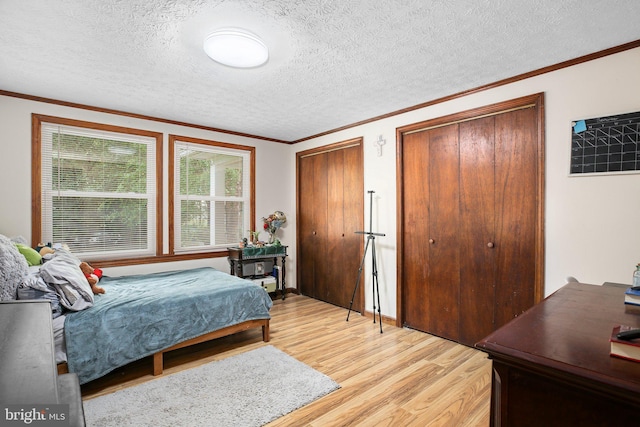 bedroom featuring light wood-type flooring, a textured ceiling, ornamental molding, and two closets