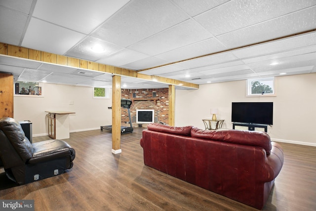 living room with a brick fireplace, plenty of natural light, and dark wood-type flooring