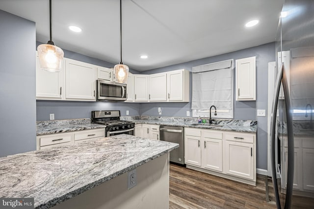 kitchen featuring appliances with stainless steel finishes, white cabinets, pendant lighting, dark hardwood / wood-style floors, and sink