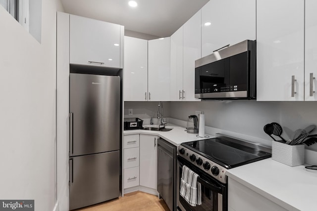 kitchen with light hardwood / wood-style flooring, sink, stainless steel appliances, and white cabinets