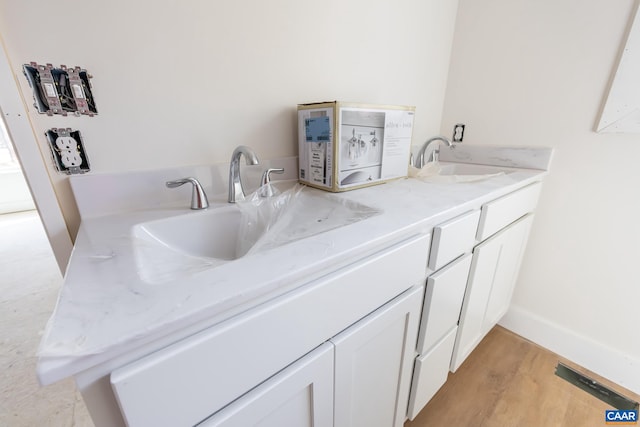 full bathroom with wood finished floors, a sink, baseboards, and double vanity