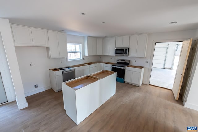 kitchen featuring stainless steel appliances, a kitchen island, white cabinets, and light wood-style floors