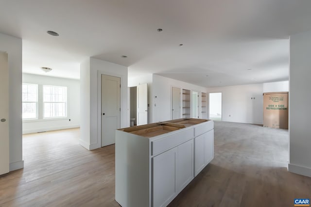 kitchen with open floor plan, a kitchen island, light wood-style flooring, and baseboards