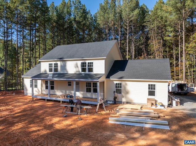 rear view of property with a shingled roof and a view of trees