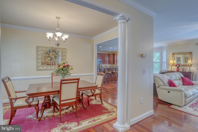 dining space with baseboards, ornamental molding, decorative columns, wood finished floors, and a notable chandelier