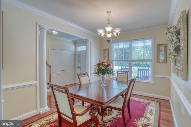 dining space featuring crown molding, a notable chandelier, light hardwood / wood-style flooring, and ornate columns