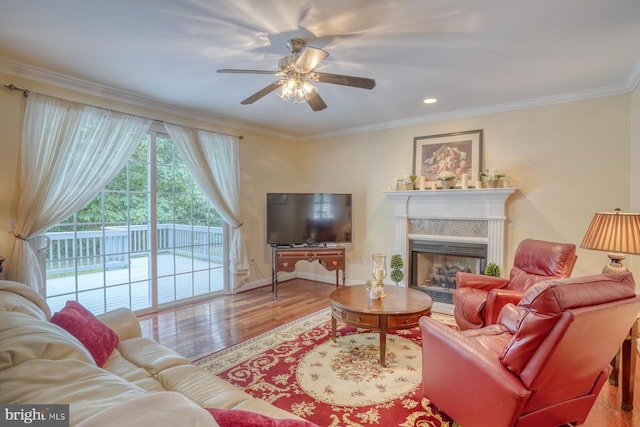 living room with wood finished floors, baseboards, a fireplace, ceiling fan, and ornamental molding