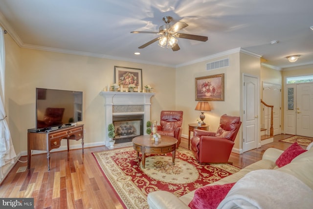 living area with visible vents, a fireplace with raised hearth, wood finished floors, crown molding, and baseboards