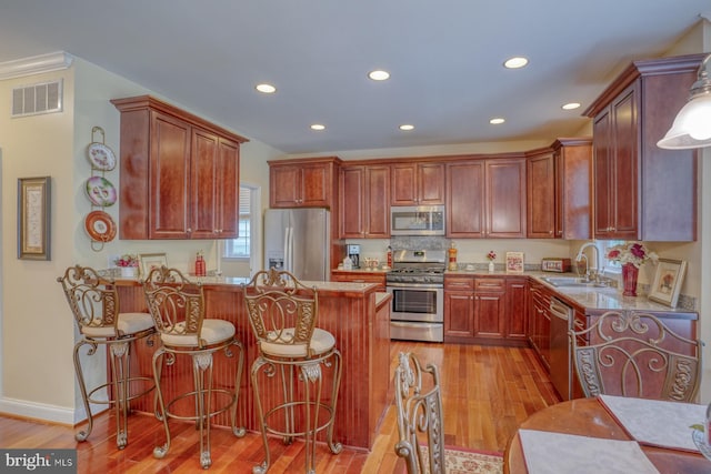 kitchen with visible vents, a sink, appliances with stainless steel finishes, a peninsula, and light wood finished floors