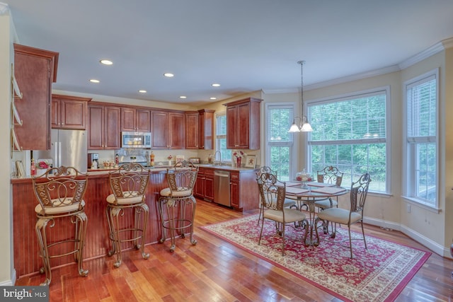 kitchen with a kitchen bar, light wood-style flooring, stainless steel appliances, a peninsula, and crown molding