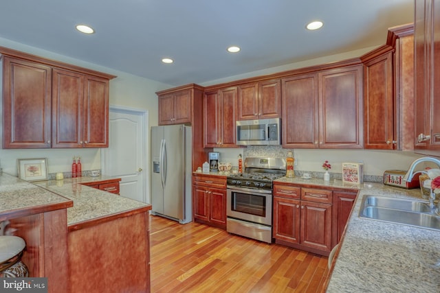 kitchen with appliances with stainless steel finishes, sink, light hardwood / wood-style floors, and kitchen peninsula