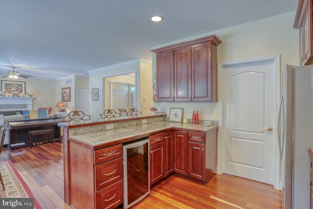 kitchen featuring wine cooler, light wood-type flooring, stainless steel refrigerator, ornamental molding, and kitchen peninsula