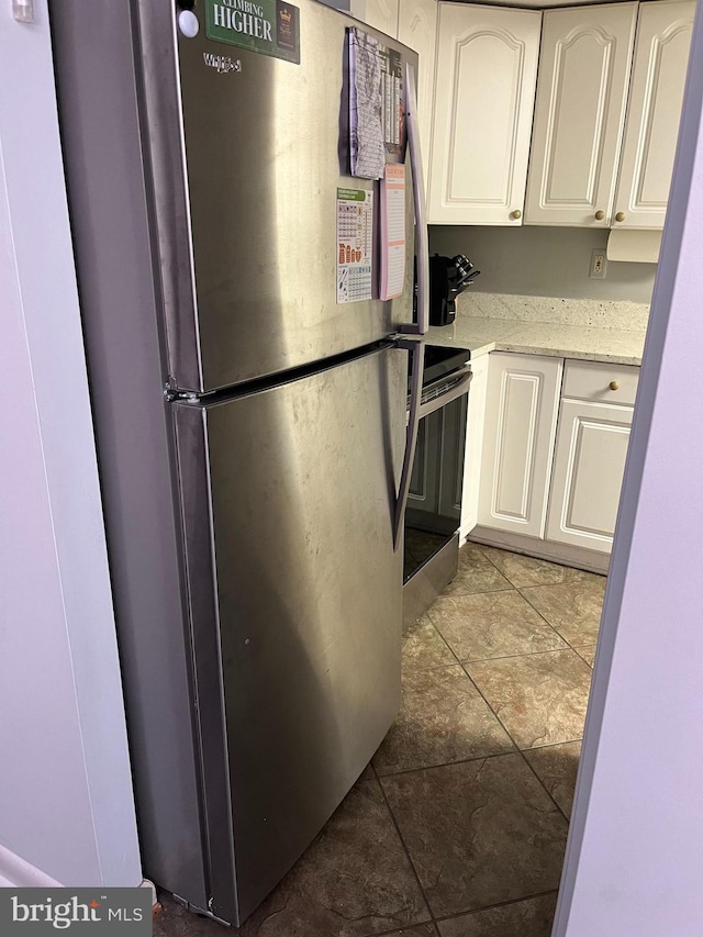 kitchen featuring light stone counters, electric stove, white cabinets, and freestanding refrigerator