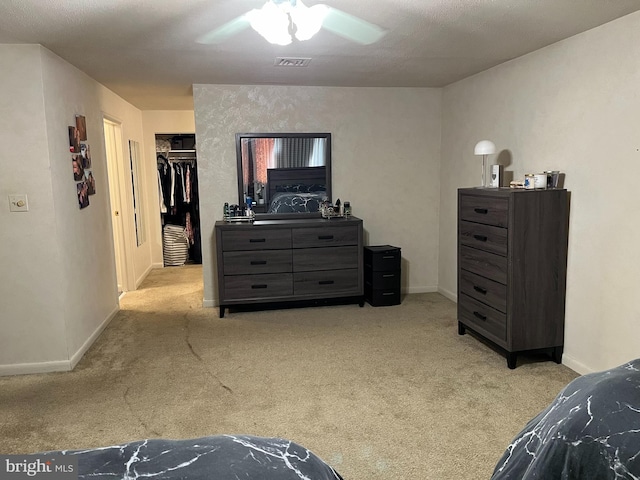 carpeted bedroom with a textured ceiling, ceiling fan, a walk in closet, and a closet