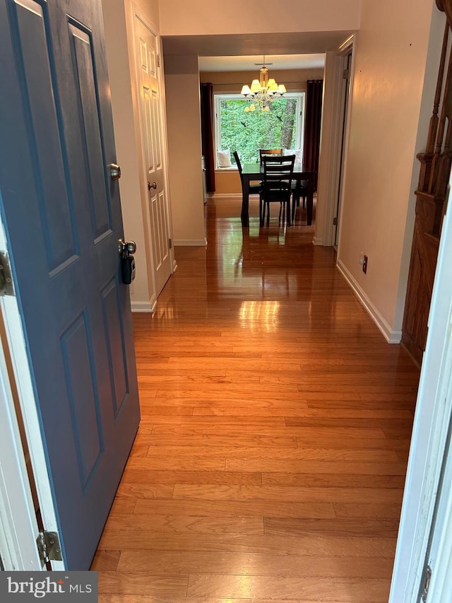 corridor with light hardwood / wood-style floors and a notable chandelier