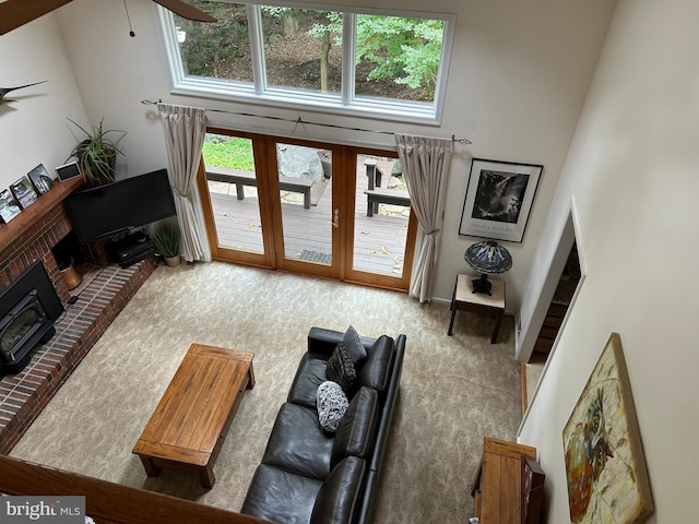 living room featuring a wood stove, a brick fireplace, ceiling fan, a towering ceiling, and carpet floors