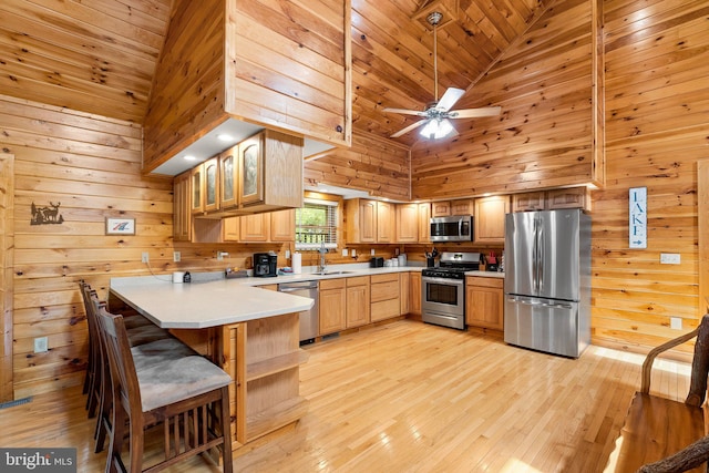 kitchen with stainless steel appliances, kitchen peninsula, high vaulted ceiling, ceiling fan, and wooden walls