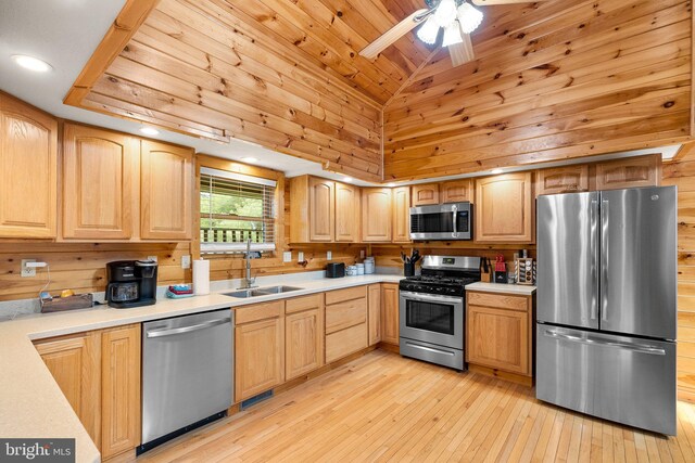 kitchen with wooden walls, stainless steel appliances, light hardwood / wood-style floors, sink, and ceiling fan