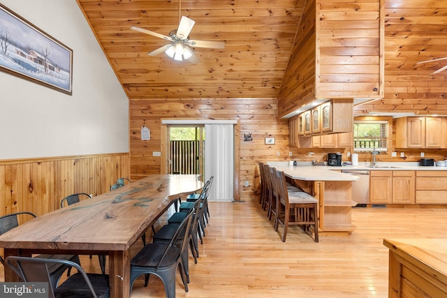 dining area with light wood-type flooring, high vaulted ceiling, wooden walls, sink, and ceiling fan