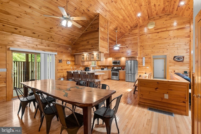 dining area with high vaulted ceiling, ceiling fan, wood walls, and light wood-type flooring