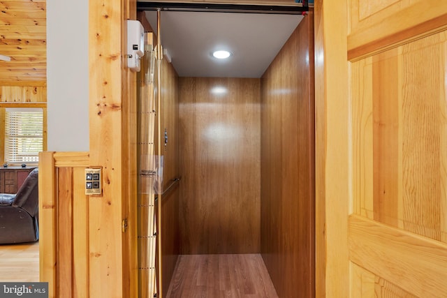 interior details featuring elevator, hardwood / wood-style floors, and wood walls