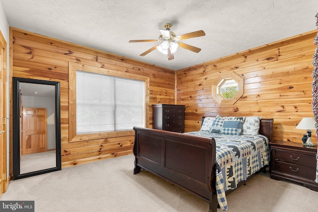 bedroom featuring a textured ceiling, light colored carpet, ceiling fan, and wooden walls