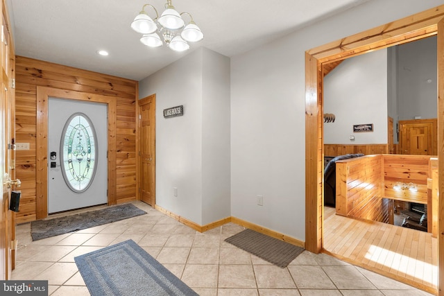 foyer with wood walls, an inviting chandelier, and light tile patterned flooring