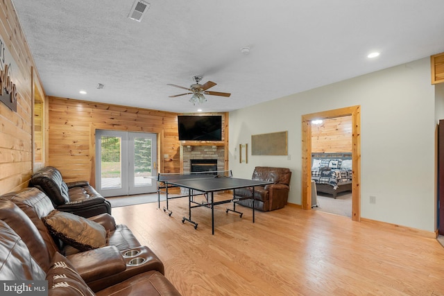 living room featuring light hardwood / wood-style floors, ceiling fan, wooden walls, and a fireplace