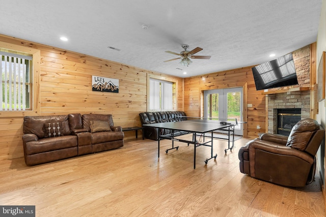 game room with light wood-type flooring, wood walls, ceiling fan, and a textured ceiling