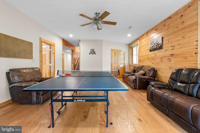 game room with ceiling fan, wood walls, and light wood-type flooring