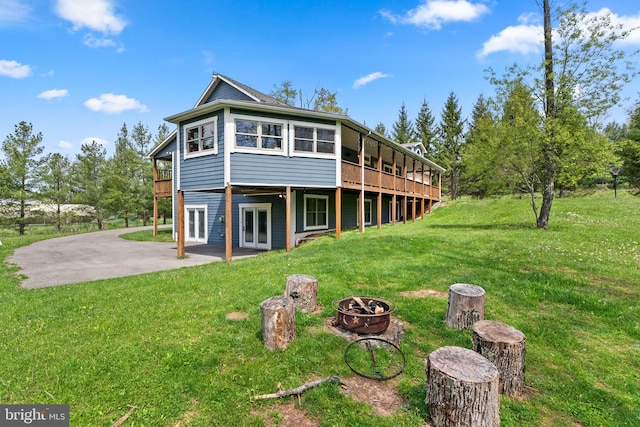 rear view of property featuring a fire pit, a wooden deck, a yard, and a patio area