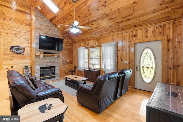 living room with a fireplace, high vaulted ceiling, a skylight, light hardwood / wood-style flooring, and ceiling fan